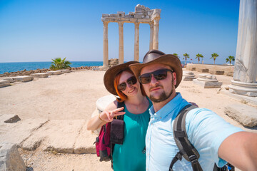 Naklejka premium A loving couple of travelers takes a selfie with a view of the ruins of the ancient Roman temple of Apollo. Sunglasses Side, Tourism and tours in Turkey.