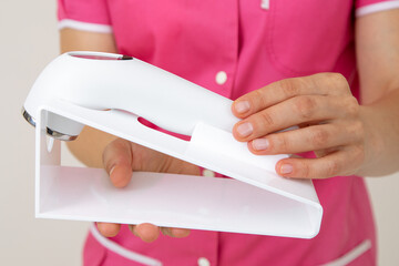 Medical worker in pink uniform holds laser device for skin care of face and body. Youth and beauty. Beauty salons. Cosmetology. Dermatology. Cosmetic procedures. Beautician tools.