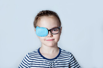 Child girl with an occluder on the eye in a striped jumper on a light background.