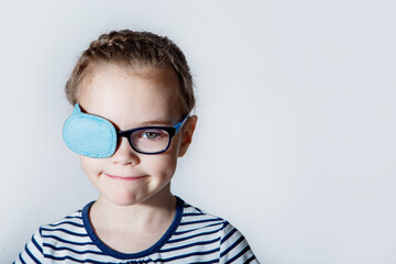 Child girl with an occluder on the eye in a striped jumper on a light background.