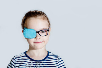 Child girl with an occluder on the eye in a striped jumper on a light background.