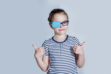 Child girl with an occluder on the eye in a striped jumper on a light background.