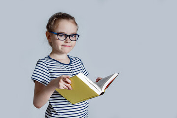 A female child in glasses with a book in her hands on a light background.
