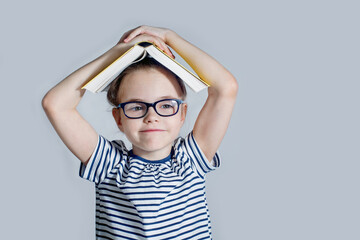 A female child with glasses holds a book above her head like a house.