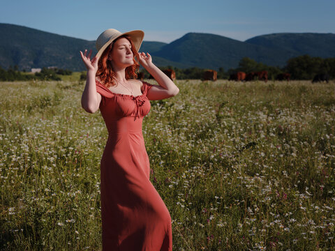 red-haired woman wearing dress and hat on summer evening field of daisies . concept of digital detox, digital cleanse, reconnecting with nature. - Powered by Adobe