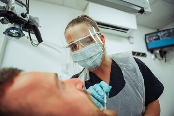 Fototapeta na wymiar Caucasian male client sitting dentist chair while female nurse operates on broken tooth