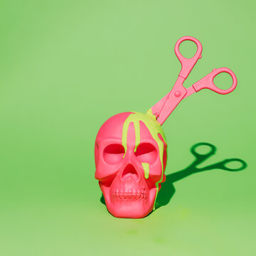 Pink human skull with scissors inside and dripping paint isolated on vivid neon green background. Creative Halloween or Day of the Dead concept. Fashion colorful retro future aesthetic.