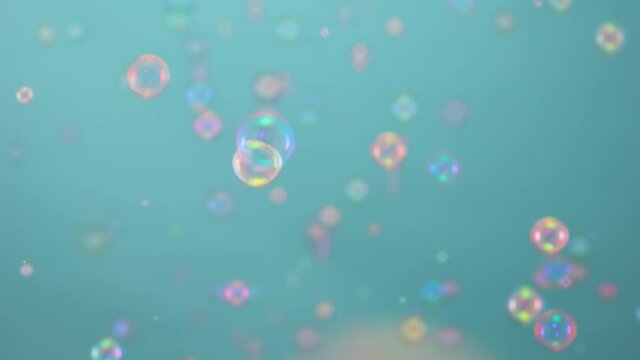 Beautiful colorful soap bubbles illuminated by pink light fly indoors on a blue background. Round bubbles float in the air and sparkle with rainbow patterns. Close up. Slow motion.
