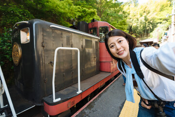 happy asian woman is taking a self portrait with the locomotive of sagano romantic train at the station on a sunny day in Arashiyama Kyoto, japan