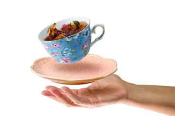 Levitating blue teacup with tea and pink saucer over the woman's hand. Isolated on a white background