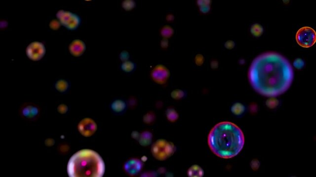 Blurred footage of beautiful colorful rainbow soap bubbles flying in the air against a black background. A lot of bubbles flying in space and shimmering in the light. Close up. Slow motion.