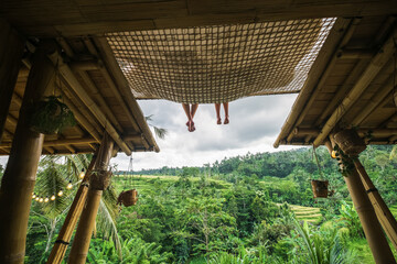 A pair of legs of a man and a woman hanging from a hammock in a villa overlooking the rice terraces.