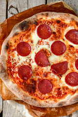 Home made italian  pepperoni   pizza with  tomatoes, mozzarella and parmesan cheese and fresh basil  on wooden background