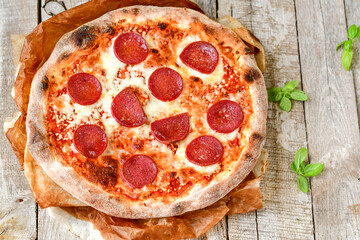 Home made italian  pepperoni   pizza with  tomatoes, mozzarella and parmesan cheese and fresh basil  on wooden background