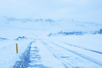 A road during a snowstorm through the lava field, Snaefellsnes Peninsula,  Iceland..Snowy Icelandic road with reflective studs. - obrazy, fototapety, plakaty