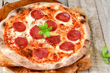 Home made italian  pepperoni   pizza with  tomatoes, mozzarella and parmesan cheese and fresh basil  on wooden background
