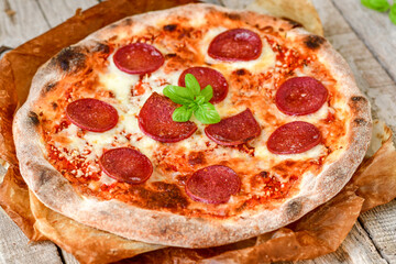 Home made italian  pepperoni   pizza with  tomatoes, mozzarella and parmesan cheese and fresh basil  on wooden background