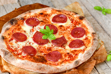 Home made italian  pepperoni   pizza with  tomatoes, mozzarella and parmesan cheese and fresh basil  on wooden background