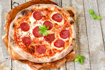 Home made italian  pepperoni   pizza with  tomatoes, mozzarella and parmesan cheese and fresh basil  on wooden background