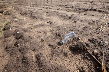 A glass bottle dumped in a plowed field.