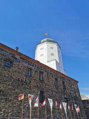 Against the blue sky, the stone wall of Vyborg Castle, flags and the white Tower of St. Olaf in the...
