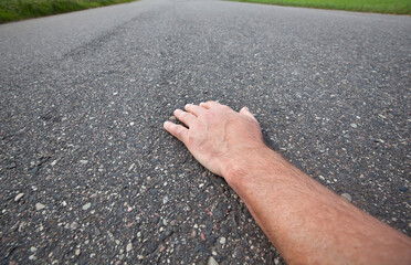 A man's hand lying on an asphalt road, perspective.