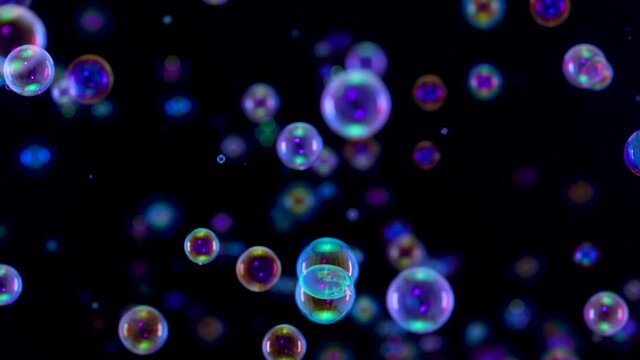 Blurred footage of beautiful blue rainbow soap bubbles flying in the air against a black background. A lot of bubbles flying in space and shimmering in the light. Close up. Slow motion.