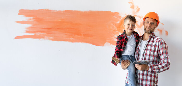 is renovating his house, the father is holding his son against the background of the wall with place for text. Father's day. Baner.