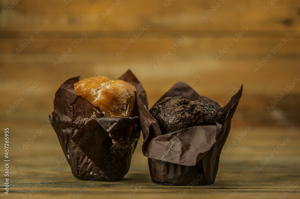 Poster Homemade chocolate and vanilla cupcakes on a wooden table, sprinkled with powdered sugar