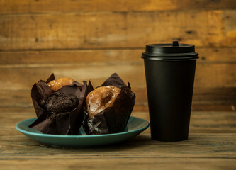 Homemade chocolate and vanilla cupcakes with paper disposable coffee cup on a wooden table, sprinkled with powdered sugar. Breakfast