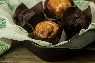 Homemade chocolate and vanilla cupcakes on a wooden table, sprinkled with powdered sugar. Breakfast