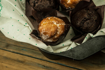 Homemade chocolate and vanilla cupcakes on a wooden table, sprinkled with powdered sugar. Breakfast