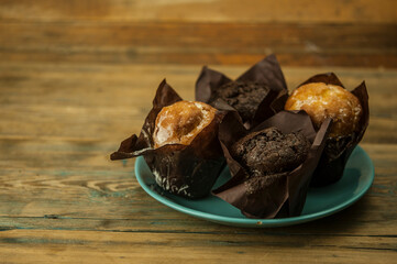 Homemade chocolate and vanilla cupcakes lie on ceramic plate on a wooden table, sprinkled with powdered sugar. Breakfast
