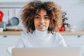 Concentrated and excited dark skinned young buyer with trendy hair looks in laptop smiles and...