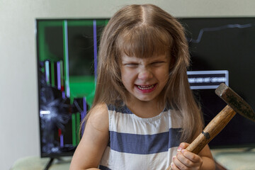 angry little girl standing in front of tv with broken screen with hammer