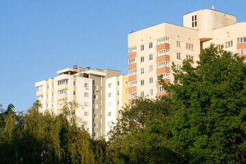 Fototapeta na wymiar Tall buildings above dense green trees in the evening sunlight.