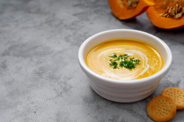 Pumpkin soup with coconut milk and squash slices. Creammy autumn soup in white bowl on gray background.