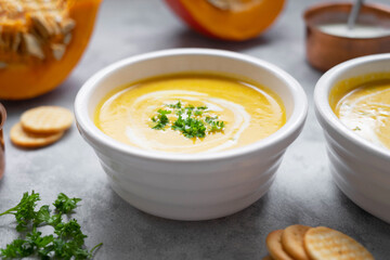 Pumpkin soup with coconut milk and squash slices. Creammy autumn soup in white bowl on gray background.