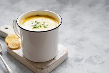 Squash or pumpkin vegan soup in metal mug. A cup of creammy autumn soup gray background with pumpkin slices.