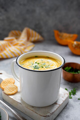 Squash or pumpkin vegan soup in metal mug. A cup of creammy autumn soup gray background with pumpkin slices.