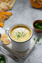 Squash or pumpkin vegan soup in metal mug. A cup of creammy autumn soup gray background with pumpkin slices.