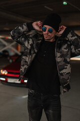 Fototapeta na wymiar fashionable young handsome man model in trendy military winter jacket with sunglasses wearing a hat in the city