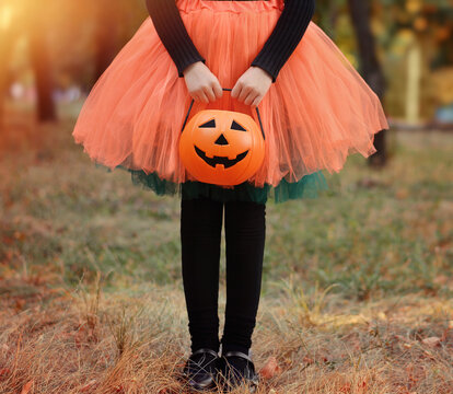 Little girl in witch costume with a pumpkin bucket . Kid having fun at Halloween trick or treat. Kids trick or treating.