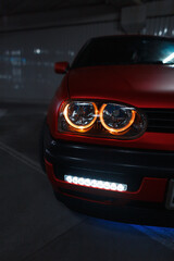 Plakat Tuned classic red car with round led headlights in the city at night