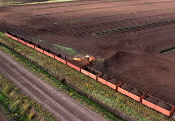 Wheel loader loads peat in freight cars. Aerial view of diesel locomotive on railroad in landscape...