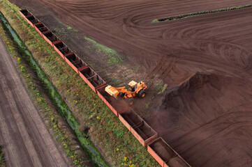 Wheel loader loads peat in freight cars. Aerial view of diesel locomotive on railroad in landscape...