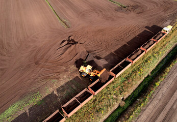 Wheel loader loads peat in freight cars. Aerial view of diesel locomotive on railroad in landscape at wetlands. Drone view of peat bog railway at peatlands. Transporting peat from peat extraction.