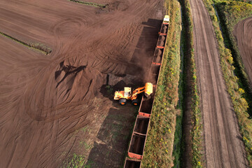 Wheel loader loads peat in freight cars. Aerial view of diesel locomotive on railroad in landscape...
