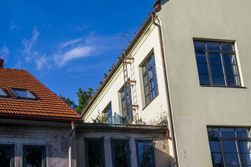 Abstract conceptual architecture of vintage roofs of houses with windows, balconies and oven and ventilation pipes against blue sky with clouds in old Town. Apartments in the attic against skyline