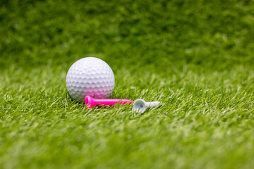 Golf ball with pink tee are on green grass